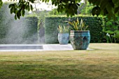 PRIVATE GARDEN, COTSWOLDS: DESIGNER ALISON HENRY - LAWN, SWIMMING POOL, BRONZE CONTAINERS WITH CORDYLINE. FORMAL, WATER, CLASSIC,  ENGLISH,  GARDEN