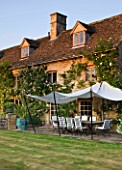 DESIGNER ALISON HENRY, PRIVATE GARDEN, COTSWOLDS - THE HOUSE WITH LAWN, STONE TERRACE / PATIO WITH SEATS AND CANVAS SAIL CANOPY - COUNTRY, GARDEN, SUMMER, CLASSIC, ENGLISH