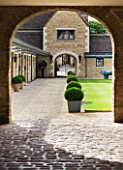 WHATLEY MANOR  WILTSHIRE: VIEW THROUGH TO THE STABLE COURTYARD WITH BOX BALLS IN METAL CONTAINERS AND LAWN
