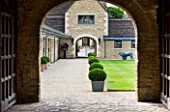 WHATLEY MANOR  WILTSHIRE: VIEW THROUGH TO THE STABLE COURTYARD WITH BOX BALLS IN METAL CONTAINERS AND LAWN
