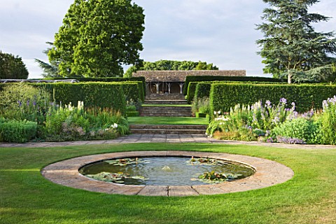 WHATLEY_MANOR__WILTSHIRE_CIRCULAR_POND_IN_THE_LAWN_WITH_VIEW_THROUGH_HEDGES_TO_THE_COTSWOLD_STONE_LO