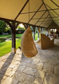 WHATLEY MANOR  WILTSHIRE: SWING SEAT/ CHAIR IN THE COTSWOLD STONE LOGGIA BUILDING WITH LAWN  POOL AND WATER FEATURE BY SIMON ALLISON