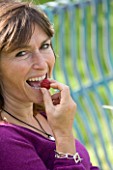 DESIGNER CLARE MATTHEWS  DEVON : FRUIT GARDEN PROJECT: CLARE EATING RASPBERRY AUTUMN BLISS ON HER BENCH IN THE FRUIT GARDEN