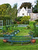 DESIGNER CLARE MATTHEWS: THE FRUIT AND VEGETABLE GARDEN IN DEVON. RAISED  BLUE PAINTED WOODEN BEDS AND ELEGANT CURVED BLUE METAL BENCH WITH THE HOUSE BEHIND