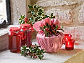 DESIGNER - JACKY HOBBS : CHRISTMAS DECORATION - CANDLES  JAM IN JARS  CHRISTMAS PUDDING WRAPPED IN RED AND WHITE CHECKED CLOTH AND HOLLY BERRIES AND LEAVES