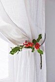 DESIGNER: JACKY HOBBS  LONDON: BEDROOM AT CHRISTMAS WITH HOLLY DECORATION TIED TO CURTAIN