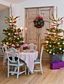 DESIGNER: JACKY HOBBS  LONDON: THE LIVING ROOM AT CHRISTMAS WITH DOOR  WREATH AND TWO CHRISTMAS TREES WITH TABLE SET WITH PINK CYCLAMEN IN CONTAINERS