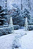 FORMAL TOWN GARDEN IN SNOW  OXFORD  WINTER: DESIGN BY LIZ NICHOLSON - PATH THROUGH GARDEN WITH WOODEN OBELISKS  YEW HEDGING  CERCIS SILIQUASTRUM AND CERCIDIPHYLLUM