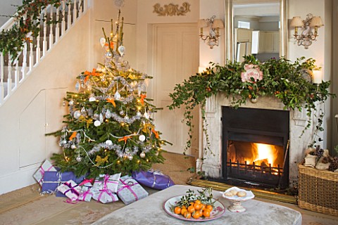 BRUERN_COTTAGES__OXFORDSHIRE_CHRISTMAS__THE_SITTING_ROOM_WITH_FIREPLACE__CHRISTMAS_TREE_AND_OTTOMAN_