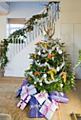 BRUERN COTTAGES  OXFORDSHIRE: CHRISTMAS - THE SITTING ROOM WITH CHRISTMAS TREE WITH PRESENTS AND STAIRCASE WITH DECORATIVE BERRY ARRANGEMENT