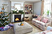 BRUERN COTTAGES  OXFORDSHIRE: CHRISTMAS - THE SITTING ROOM WITH CHRISTMAS TREE SURROUNDED BY PRESENTS  FIREPLACE AND OTTOMAN WITH BOWL OF SATSUMAS