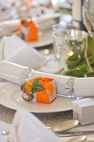 BRUERN_COTTAGES__OXFORDSHIRE_CHRISTMAS__PLACE_SETTING_WITH_CRACKER_AND_PRESENT_WRAPPED_IN_ORANGE_RIB