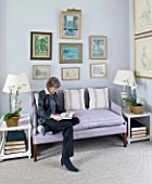 DESIGNER JANE CHURCHILL : THE DRAWING ROOM - JANE SITS ON A SOFA WITH SOME OF HER FAVOURITE PAINTINGS HUNG ABOVE