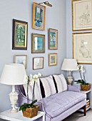 DESIGNER JANE CHURCHILL : THE DRAWING ROOM - FAVOURITE PAINTINGS HUNG ABOVE A SOFA IN PRINTED COTTON BY TISSUS DHELENE. CUSHIONS FOUND AT BATTERSEA ANTIQUES FAIR