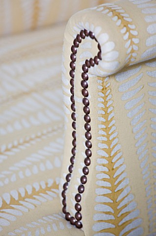 DESIGNER_JANE_CHURCHILL__STUD_DETAIL_ON_ARM_OF_UPHOLSTERED_CHAIR_IN_THE_DRAWING_ROOM