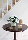 DESIGNER CLARE MATTHEWS - HOUSEPLANT PROJECT - WHITE AZALEA IN A WICKER CONTAINER ON A TABLE IN HALLWAY BESIDE STAIRS