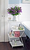 DESIGNER: KALLY ELLIS  LONDON: PURPLE CLEMATIS CUT FLOWERS IN ENAMEL JUG IN BATHROOM BESIDE BATH