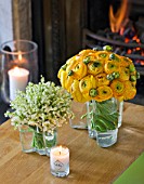 DESIGNER: KALLY ELLIS  LONDON: GLASS VASES HOLD LILY-OF-THE-VALLEY AND RANUNCULUS BLOOMS; FRAGRANT MCQUEENS CANDLE. FIRE IN BACKGROUND