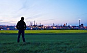 TEESSIDE  UNITED KINGDOM - BOY WITH HOODIE LOOKING AT PETROCHEMICAL WORKS AT DUSK SEEN FROM FIELD OF RAPESEED - INDUSTRY  OIL INDUSTRY  INDUSTRIAL  HEAVY INDUSTRY