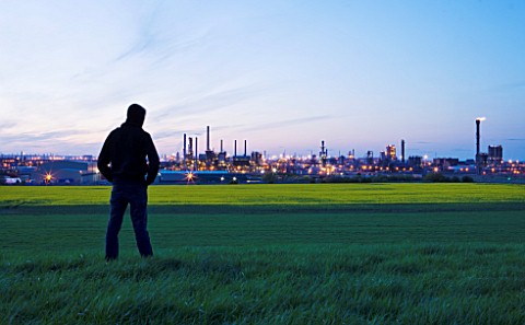 TEESSIDE__UNITED_KINGDOM__BOY_WITH_HOODIE_LOOKING_AT_PETROCHEMICAL_WORKS_AT_DUSK_SEEN_FROM_FIELD_OF_