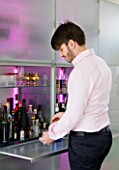 CAKE BOY HOUSE  LONDON: ERIC LANLARD MAKING DRINKS ON THE SLIDE- OUT PANEL OF THE LED LIT FROSTED GLASS STORAGE CABINET BY EO  IN THE LIVING ROOM