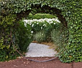 LE JARDIN DALCHIMISTE  PROVENCE  FRANCE; DESIGNERS  ERIC OSSART AND ARNAUD MAURIERES: METAL CIRCLE THROUGH  HEDGE TO WHITE ICEBERG ROSES IN THE WHITE SQUARE