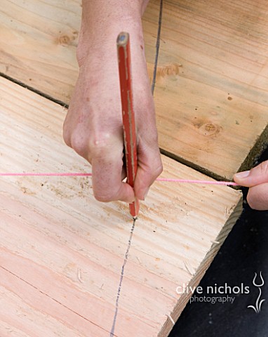 DESIGNER_CLARE_MATTHEWS__DECKING_PROJECT__PENCIL_MARKING_OUT_WHERE_TO_CUT_DECK_BOARDS