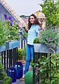 THE BALCONY GARDENER - ISABELLE PALMER WATERING A DELPHINIUM ON HER BALCONY