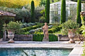 DESIGNER MICHEL SEMINI  PROVENCE  FRANCE: MAS THEO - THE SWIMMING POOL GARDEN WITH STATUE OF NEPTUNE  IRISES AND PARTERRE OF CLIPPED TEUCRIUM FRUTICANS AND SANTOLINA - GREENHOUSE