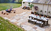 DESIGNER: CLARE MATTHEWS  DEVON - PAVING PROJECT - PATIO WITH TABLE AND CHAIRS AND GRAVEL SEATING AREA WITH LARGE SQUARE WOODEN BLOCKS FOR SEATS AND FIRE CAULDRON