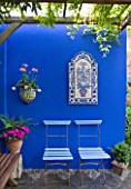 KARLA NEWELL GARDEN  BRIGHTON: SMALL TOWN GARDEN - BLUE CAFE CHAIRS BESIDE BLUE PAINTED WALL WITH PERGOLA ABOVE