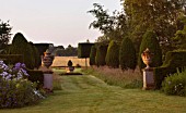 KINGSBRIDGE FARM  BUCKINGHAMSHIRE: FORMAL YEW AVENUE WITH URNS AND MEADOW GRASS - CENTRAL FONT AND PLEACHED HORNBEAM  FARMLAND BEYOND