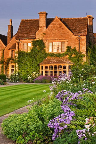 WHATLEY_MANOR__WILTSHIRE_VIEW_OF_THE_HOTEL_ACROSS_THE_LAWN_AND_HERBACEOUS_BORDER_AT_SUNSET