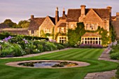 WHATLEY MANOR  WILTSHIRE: VIEW OF THE HOTEL ACROSS THE LAWN AND HERBACEOUS BORDERS   AT SUNSET