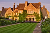 WHATLEY MANOR  WILTSHIRE: VIEW OF THE HOTEL ACROSS THE LAWN AND HERBACEOUS BORDERS   AT SUNSET