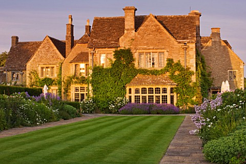 WHATLEY_MANOR__WILTSHIRE_VIEW_OF_THE_HOTEL_ACROSS_THE_LAWN_AND_HERBACEOUS_BORDERS___AT_SUNSET