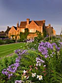 WHATLEY MANOR  WILTSHIRE: VIEW OF THE HOTEL ACROSS THE LAWN AND HERBACEOUS BORDER AT SUNSET. LILIUM REGALE IN FOREGROUND