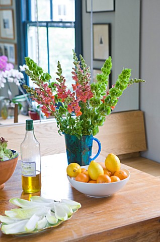 CHANTAL_COADY_HOUSE__LONDON_THE_DINING_ROOM_WITH_MIRRORED_CUPBOARDS_BEHIND__SNAPDRAGONS_IN_VASE__BAL