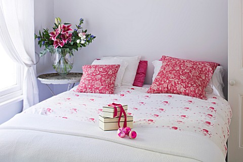 DESIGNER_JACKY_HOBBS__LONDON__WHITE_BEDROOM_AT_CHRISTMAS_WITH_PRESENT_ON_BED_AND_RED_PILLOWS