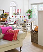JACKY HOBBS HOUSE  LONDON: RICH AUTUMN FLOWERS IN THE COOL GREY SITTING ROOM ; BRIGHT DAHLIAS  CUSHIONS AND THROWS. DINING TABLE SET WITH FLOWERS FOR SEASONAL SUPPER. LOG FIRE.