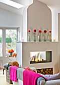 JACKY HOBBS HOUSE  LONDON: THE LIVING ROOM WITH PINK AND GREY THROWS OVER SOFA  FIRE WITH DAHLIAS IN GLASS BOTTLES ON MANTELPIECE
