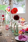 JACKY HOBBS HOUSE  LONDON: AUTUMN TABLE DECORATED WITH VINTAGE GLASS BOTTLES EACH HOLDING A BRIGHT DAHLIA