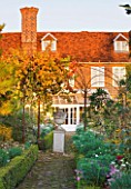 SALING HALL  ESSEX:  BRICK PATH LEADING TO HOUSE AND CONSERVATORY WITH URN ON PLINTH AND VINE IN AUTUMN COLOUR - EVENING LIGHT