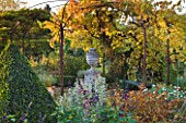 SALING HALL  ESSEX:  TOPIARY PYRAMID  METAL PERGOLA WITH URN ON PLINTH AND VINE IN AUTUMN COLOUR - EVENING LIGHT
