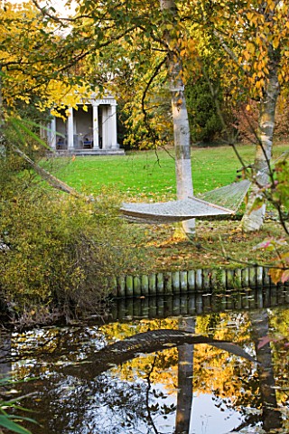 SALING_HALL__ESSEX_AUTUMNAL_VIEW_ACROSS_POND_TO_TEMPLE_OF_PISCES_WITH_HAMMOCK_IN_FIREGROUND_SLUNG_BE