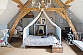 ROQUELIN  LOIRE VALLEY  FRANCE: CHILDS ROOM: EAVED AND BEAMED BEDROOM WITH CENTRAL CANOPIED METAL FRAME BED WITH VINTAGE QUILT AND DECORATIVE CANDELABRA