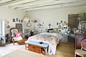 ROQUELIN  LOIRE VALLEY  FRANCE: MASTER BEDROOM; WITH PALE WOODEN CEILING BEAMS AND WOODEN FLOOR  WALLS DECORATED WITH PERSONAL ARTEFACTS  MEMENTOES AND PHOTOGRAPHS