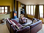 RICKYARD BARN HOUSE  OXFORDSHIRE: DESIGNERS JANE AND CLIVE NICHOLS. LIVING ROOM WITH WOOD BURNING FIRE AND LEATHER SOFAS