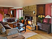 RICKYARD BARN HOUSE  OXFORDSHIRE: DESIGNERS JANE AND CLIVE NICHOLS. LIVING ROOM WITH WOOD BURNING FIRE  SOFAS  COFFEE TABLE AND RED WALLS