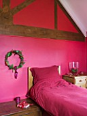 RICKYARD BARN HOUSE  OXFORDSHIRE: DESIGNERS JANE AND CLIVE NICHOLS. BEDROOM PAINTED RICH PINK/ RED WITH WREATH ON WALL - CHRISTMAS